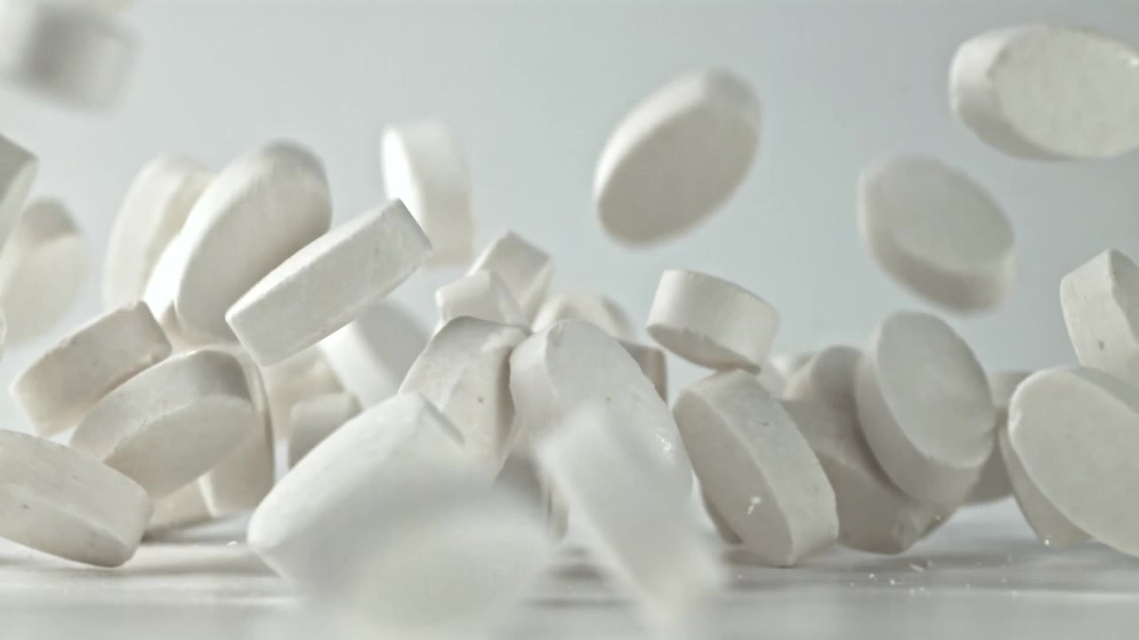Pillole mediche bianche in caduta rallentata su sfondo bianco