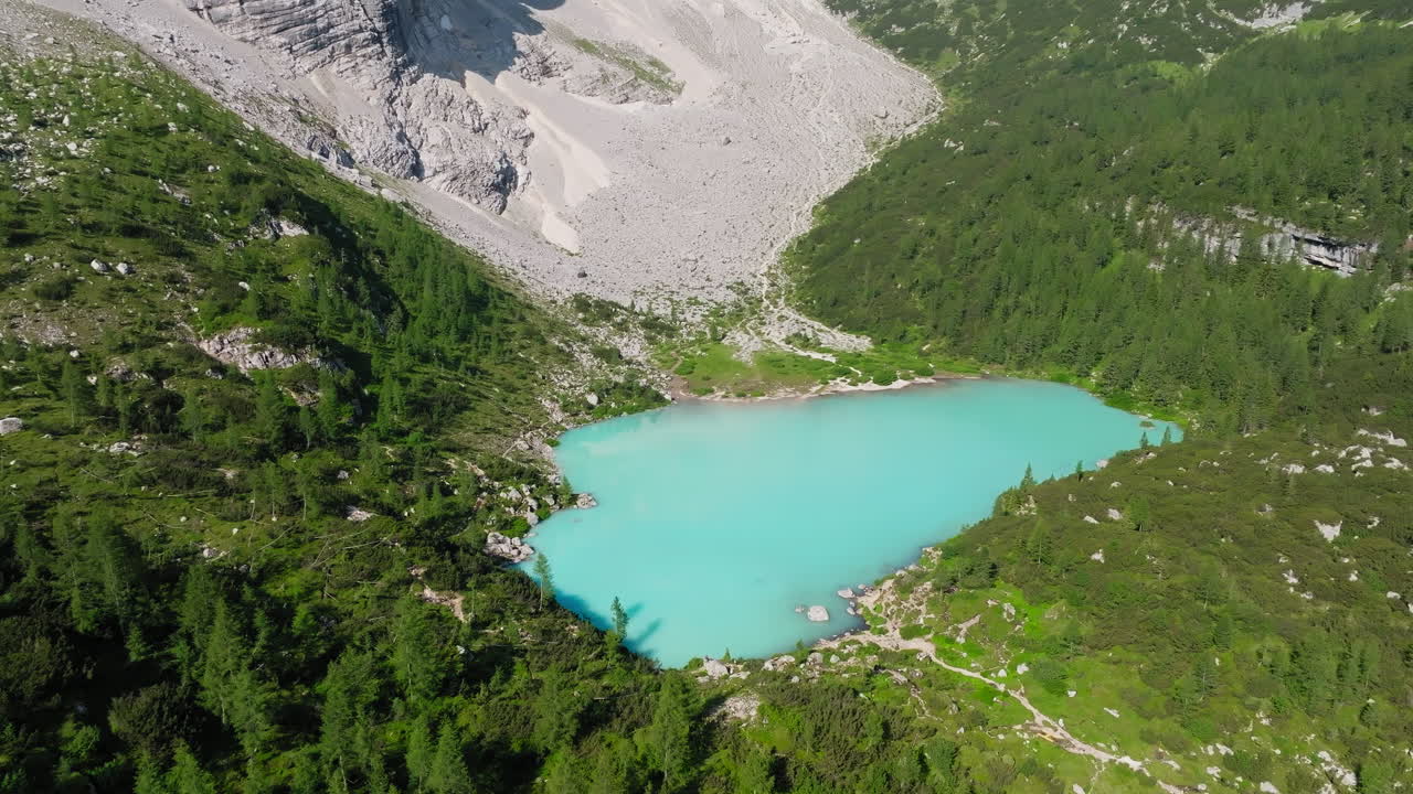 Aerial view of Lake Sorapis in the Italian Dolomites during spring, featuring its iconic turquoise waters surrounded by melting snow and awakening alpine landscapes