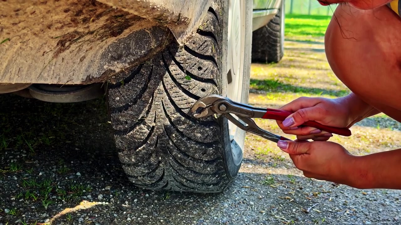 Person using pliers and hand tools to remove object from car tire outdoors