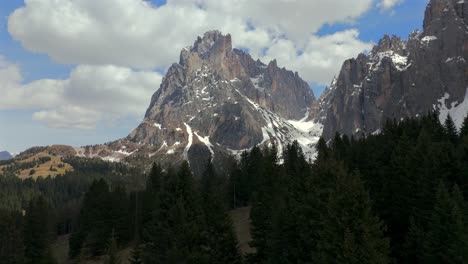 stunning view of the sassolungo mountain with snow-capped peaks rising above a dense pine forest in the dolomites under a vibrant blue sky