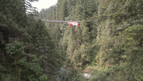 Visitors-walking-on-suspension-bridge-with-Canadian-flag,-wide-shot