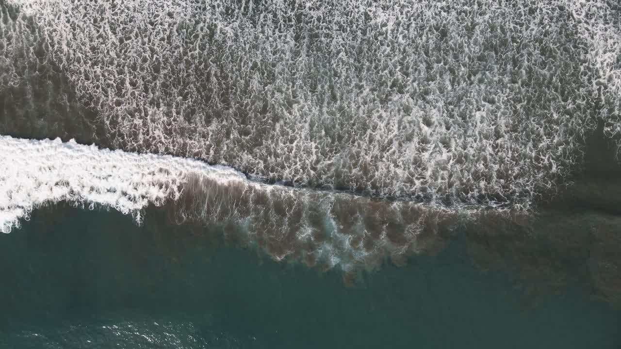 Aerial view of waves crashing upon shore in Dominical Beach in Costa Rica, bird eye wide shot