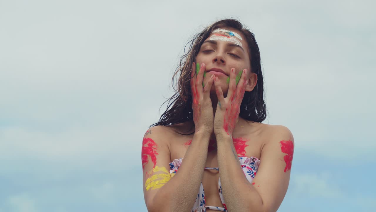A girl wearing body paint and a bikini enjoys the sun on a white sand beach in the Caribbean facial close up