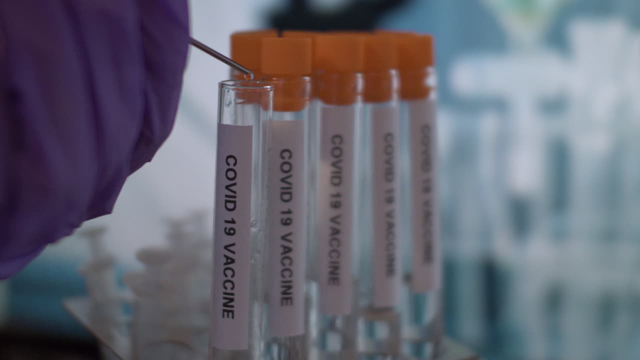 punta de jeringa que gotea la vacuna contra el coronavirus covid 19 en un vial de tubo de ensayo