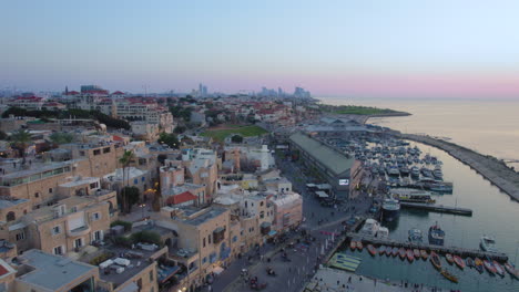 Altstadt-Von-Jaffa-Und-Jaffa-Hafen-Bei-Sonnenuntergang-Mit-Vielen-Familien,-Die-Restaurants,-Geschäfte-Und-Bars-Im-Hafen-Besuchen-–-Parallaxen-Drohnenaufnahme