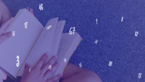 una estudiante está sentada en el suelo en una biblioteca y leyendo un libro