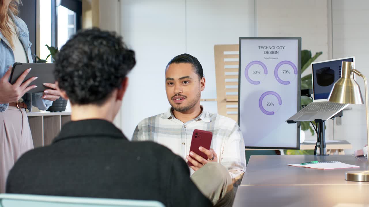 Diverse coworkers entering meeting room to discuss progress, man scrolling phone pointing to charts