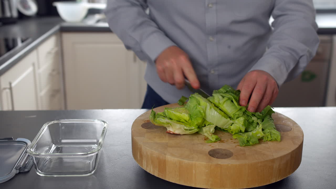 A man chopping fresh lettuce on a round wooden cutting board in a modern kitchen