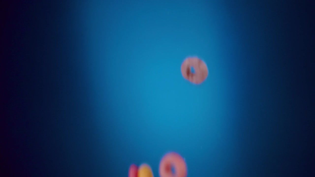 cereales de desayuno bucles frutales que caen en movimiento lento con fondo azul