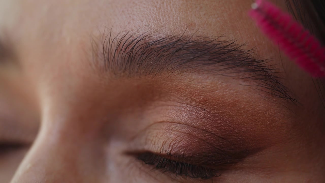 Woman making eyebrow makeup using pink small cosmetic brush in bathroom closeup.