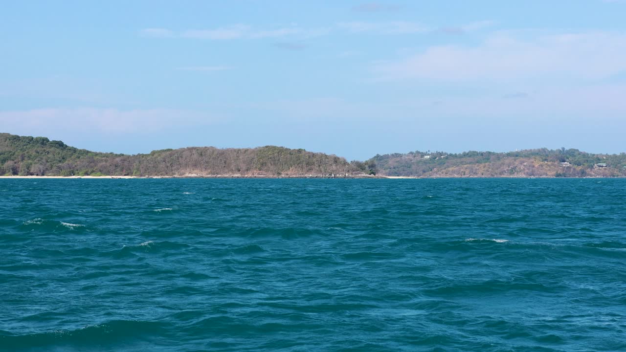 Gentle waves roll under a clear sky near Phuket, Thailand. The tranquil scene captures the island's natural beauty and calm atmosphere