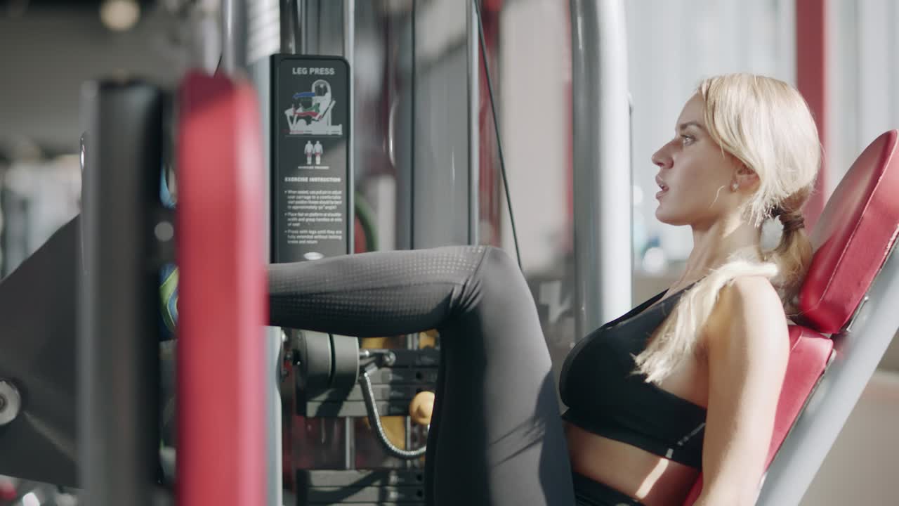 Pretty fitness girl training leg press on machine in sport club.