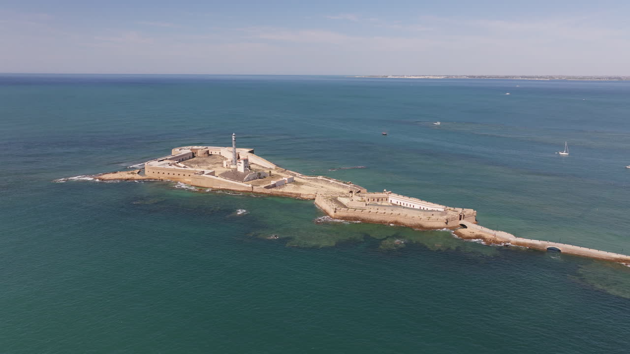 İspanya, Endülüs, Cadiz kıyısındaki San Sebastian Kalesi ve deniz fenerinin Atlantik Okyanusu ile çevrili olduğu güneşli bir günde havadan drone görüntüsü. Tarihi ada kalesi simgesi.