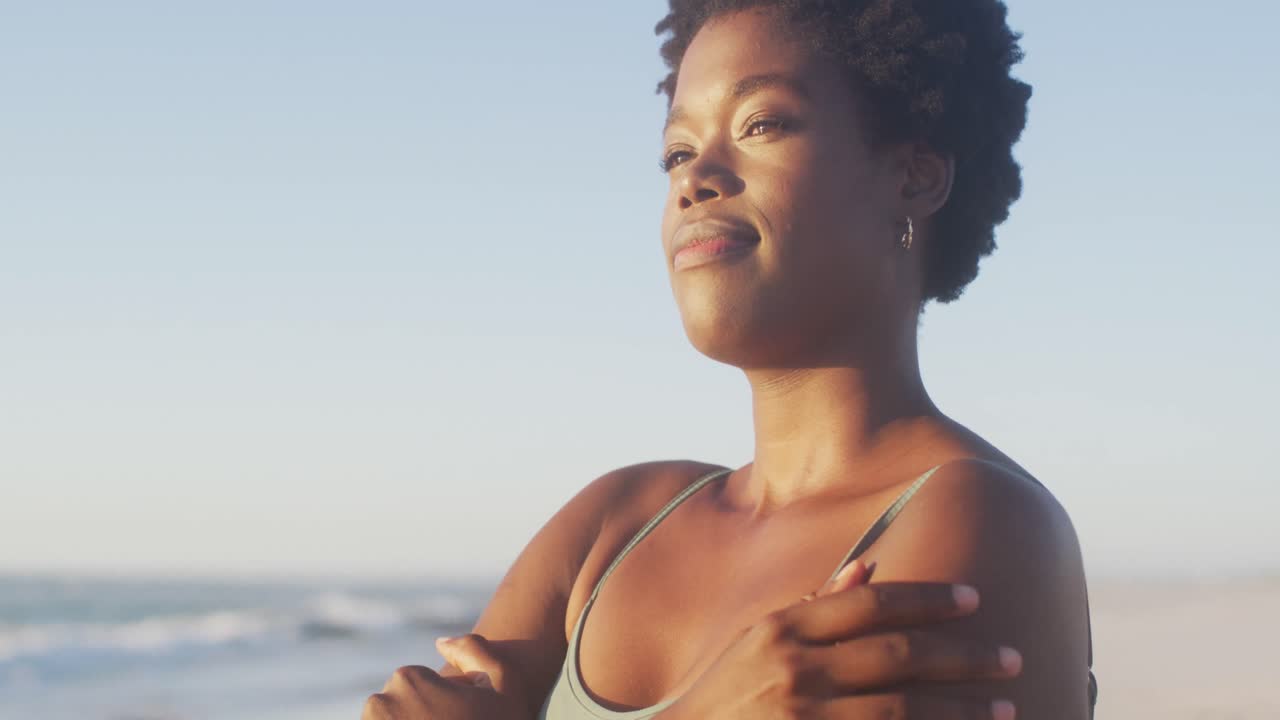 Vidéo d'une femme afro-américaine debout sur la plage au coucher du soleil