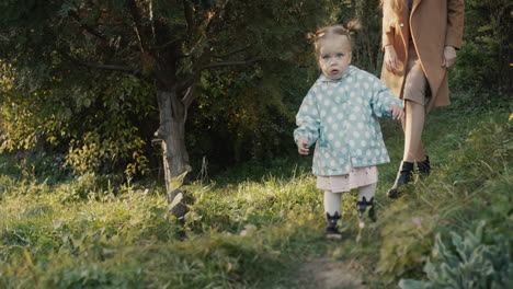 mom walks with her little daughter in the park, the girl runs ahead of her mother