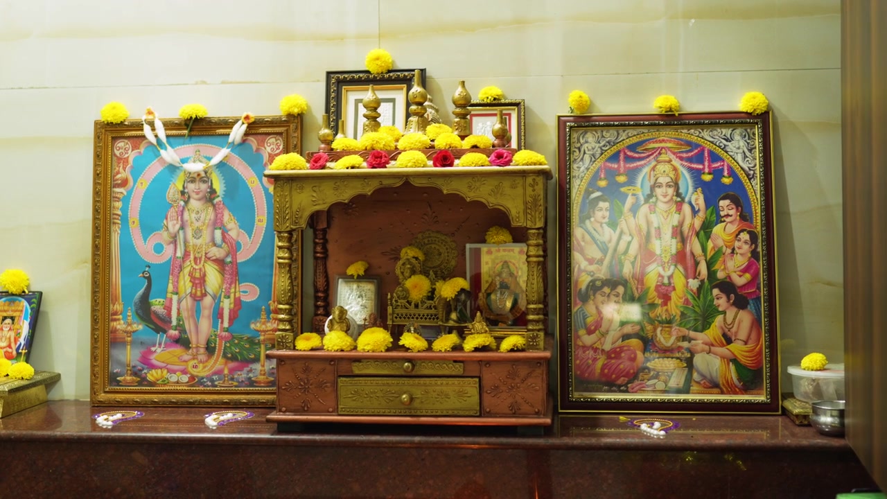 Colorful South Indian pooja room shrine with framed deities and yellow flowers arranged on a wooden altar.