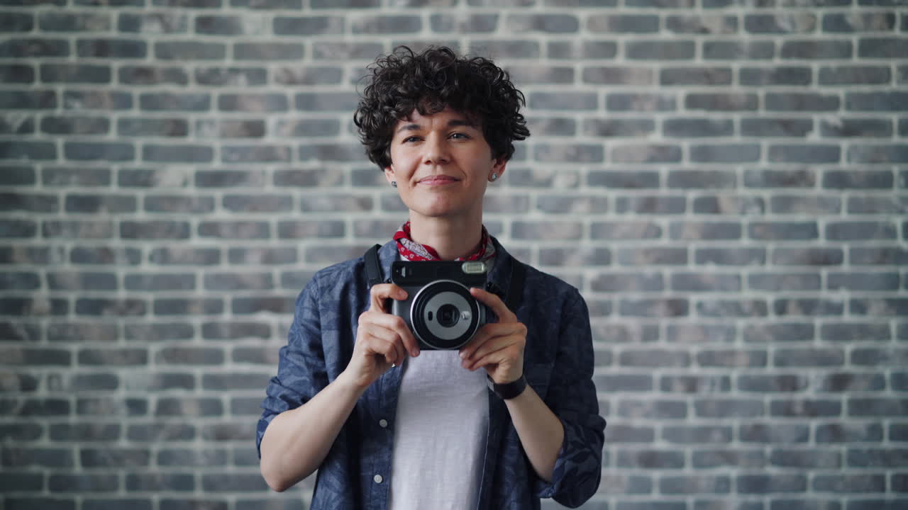 Giovane con macchina fotografica istantanea davanti a un muro di mattoni