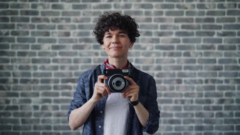 young person with instant camera in front of brick wall