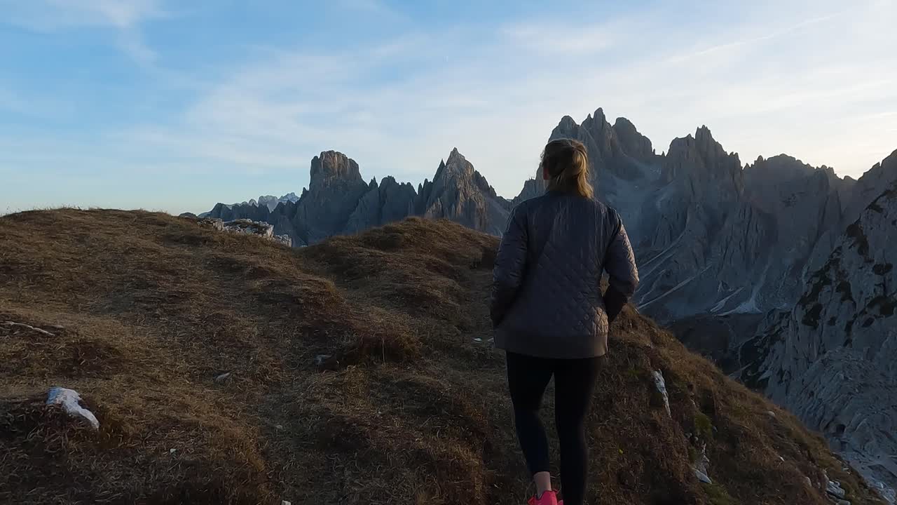 Zadní sledování ženy na túře, zatímco slunce zapadá za Dolomity, podsvícený horský výhled