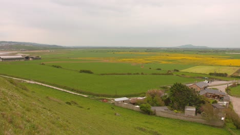 Countryside-Landscape-Of-Large-Field-With-Green-Grasses-And-House-In-Somerset,-England