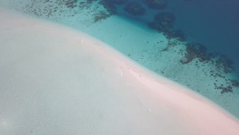 pareja de turistas en un islote arenoso en el mar de coral: antena giratoria ascendente