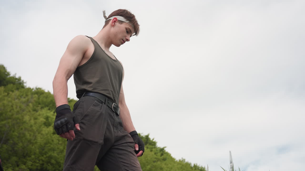 tourist descending steep grassy slope toward riverbank with cautious steps wearing fingerless gloves and tank top under cloudy sky in serene wilderness setting highlighting outdoor adventure spirit