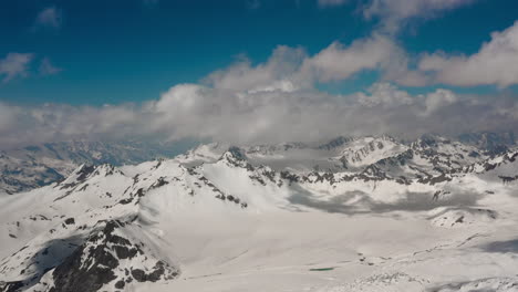 Air-flight-through-mountain-clouds-over-beautiful-snow-capped-peaks-of-mountains-and-glaciers.