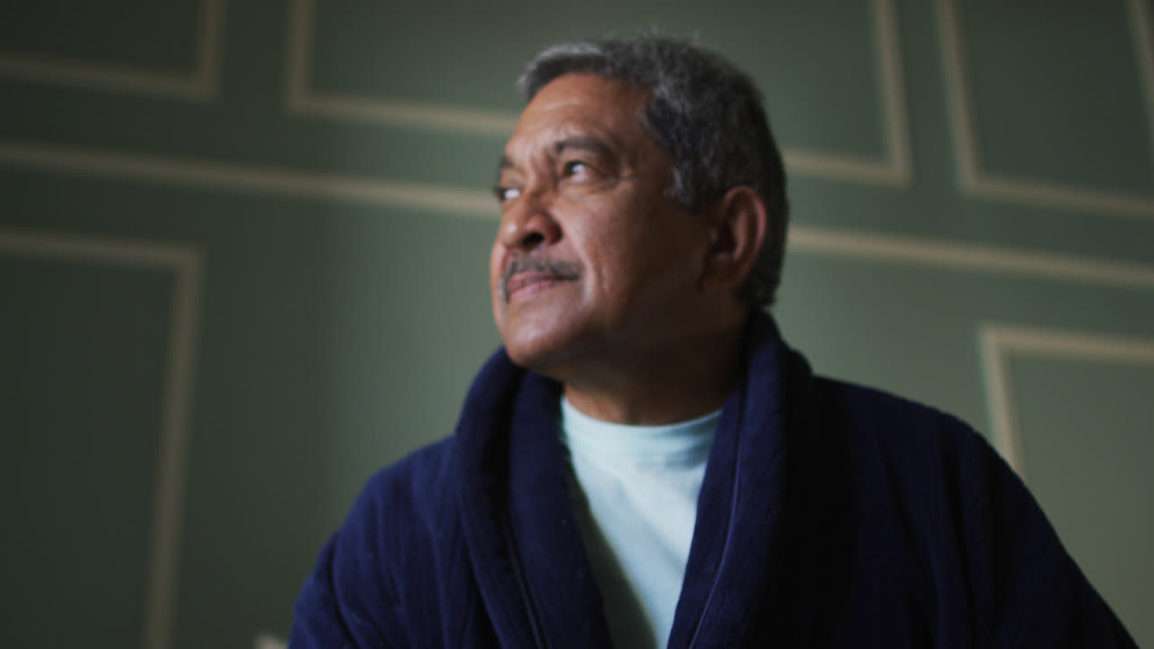 hombre de raza mixta mayor con bata de vestir mirando hacia otro lado sonriendo