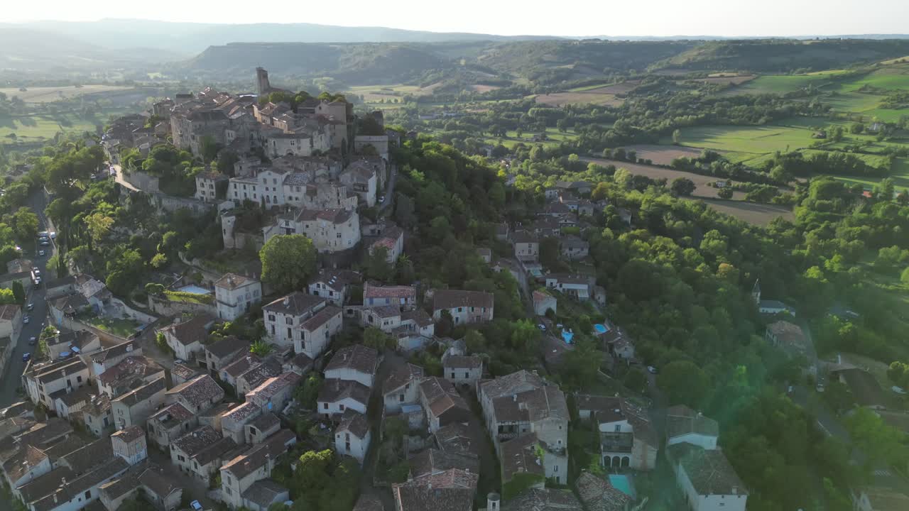 Drone aerial view in France countryside small old medieval brick town on a mountain top surrounded by green fields vertical ascend on a sunny day in Cordes Sur Ciel