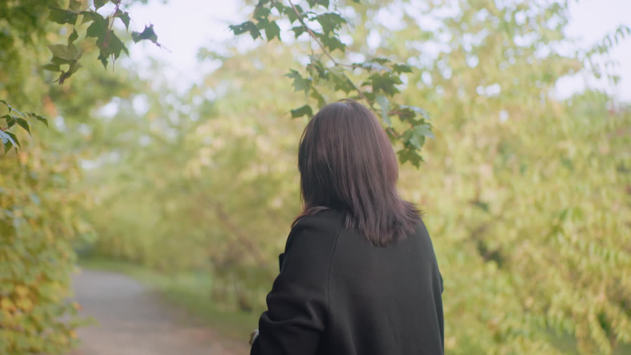 가을을 사랑하는 여성이 숲길을 거닐며 캐노피 그늘을 바라보고, 푸른 잎 아래에서 천천히 걷고, 평온한 분위기, 부드러운 보케 배경, 조용한 공원 분위기, 사색에 잠긴 자연의 순간