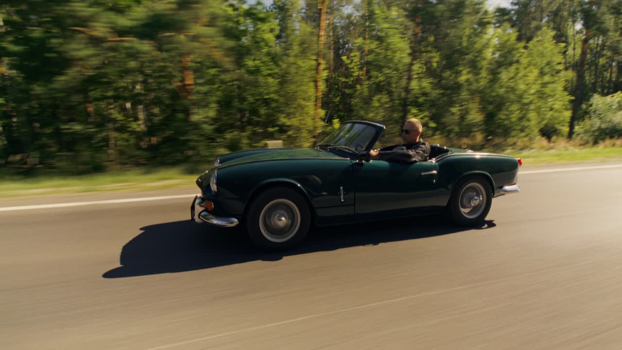 A man drives a green convertible car on a road