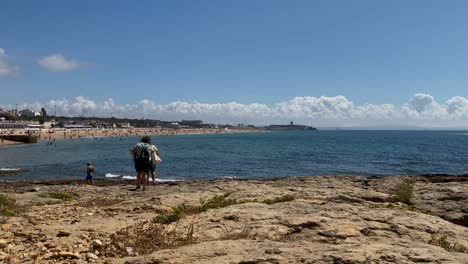 Panoramablick-Auf-Meereswellen,-Die-Zusammenbrechen,-Und-Menschen,-Die-Am-Strand-Entlang-Spazieren