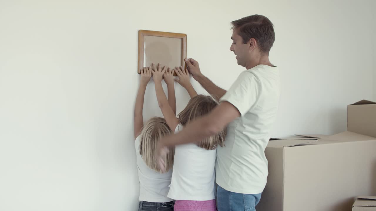 dos niñas y su padre eligiendo un lugar en la pared para la imagen