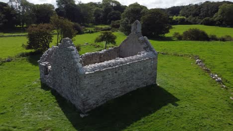 Aerial-view-circling-Capel-Lligwy-ruined-chapel-on-Anglesey-island-coastline,-North-Wales