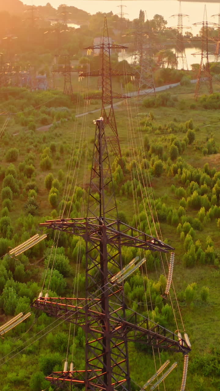 Power line pylons near the river. Electric towers with electric cables with high voltage current. Flight over the transmission lines in the evening. Aerial view. Vertical video