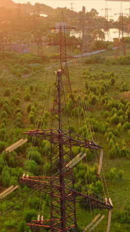 power line pylons near the river. electric towers with electric cables with high voltage current. flight over the transmission lines in the evening. aerial view. vertical video
