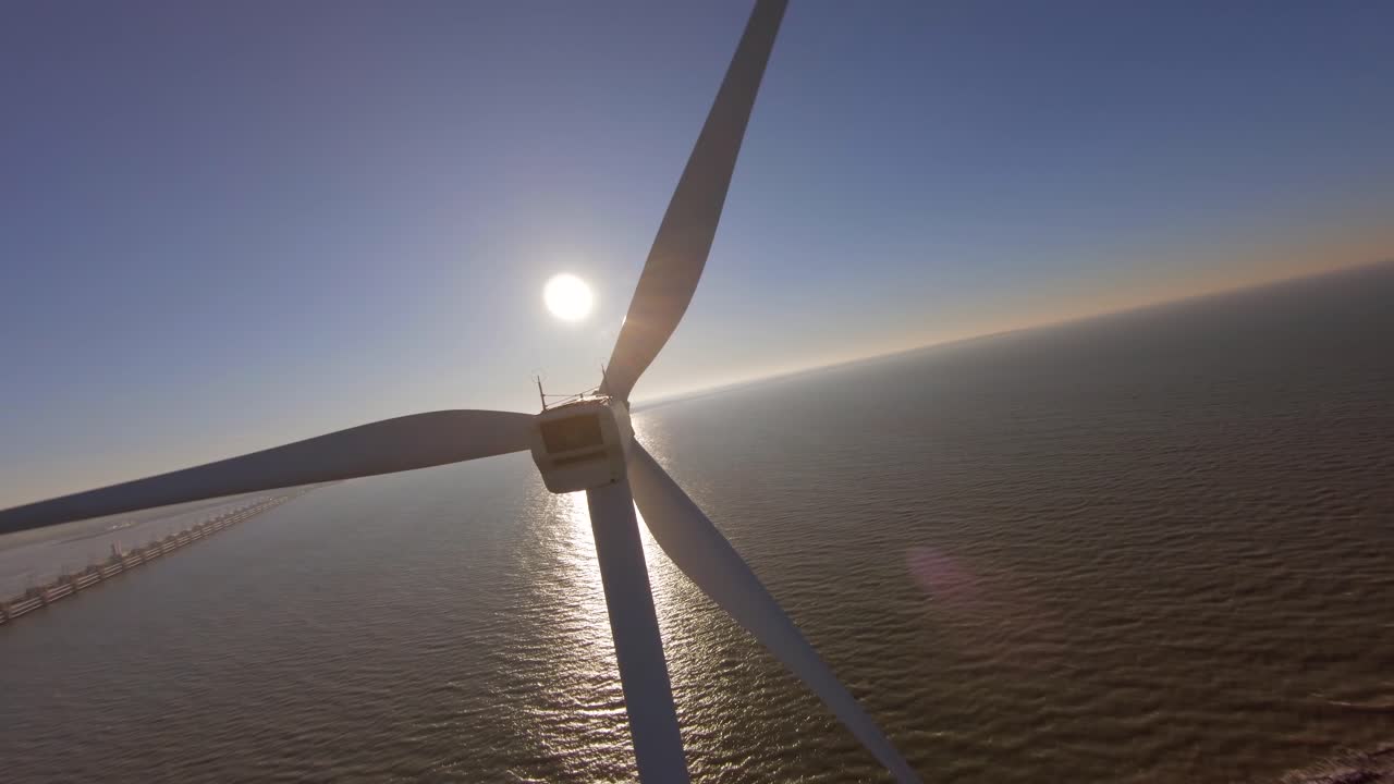 Orbit close to a large windturbine on a dyke in the middle of the sea during sunset