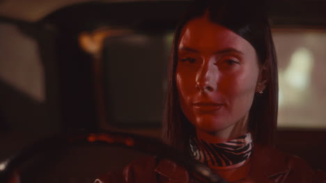 portrait of beautiful woman with red lips driving retro car at night