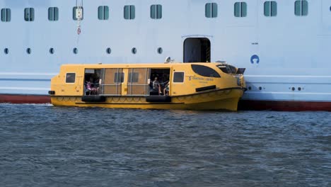 yellow lifeboat with passengers docking at a cruise ship