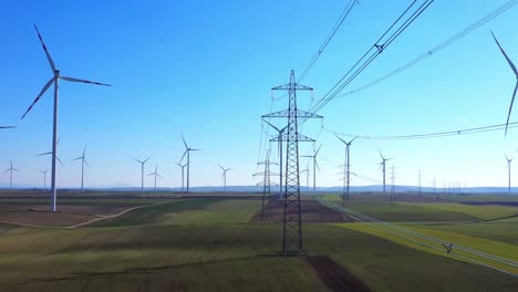 scenic view of rotating wind turbines and stream mast against blue sky in green fields