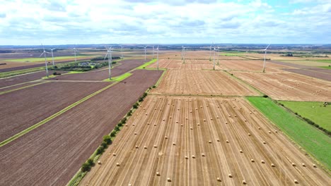 arriba, un video aéreo revela una vista cautivadora: turbinas eólicas girando con gracia en el campo recientemente cosechado de un agricultor de lincolnshire, con balas de heno doradas en primer plano