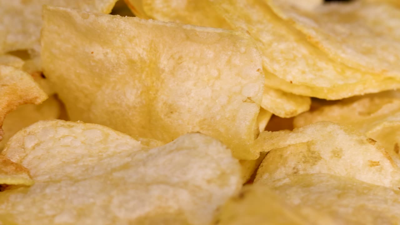 Golden potato chips rotate in close-up against black background, crisp texture highlighted by studio lighting