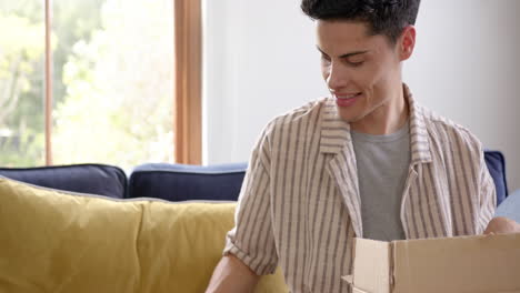 happy biracial man opening delivery in cardboard box and using smartphone, slow motion