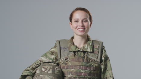 studio portrait of smiling young female soldier in military uniform against plain background