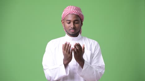 young handsome african man wearing traditional muslim clothes against green background