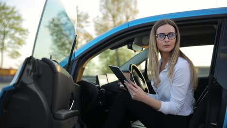 a woman sits in the seat of an electric car with a tablet. beautiful business woman