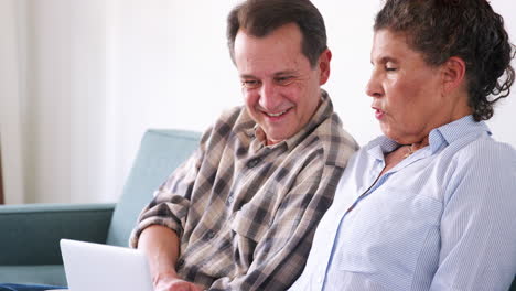 Senior-Couple-Sitting-On-Sofa-At-Home-Using-Laptop-Computer-To-Shop-Online