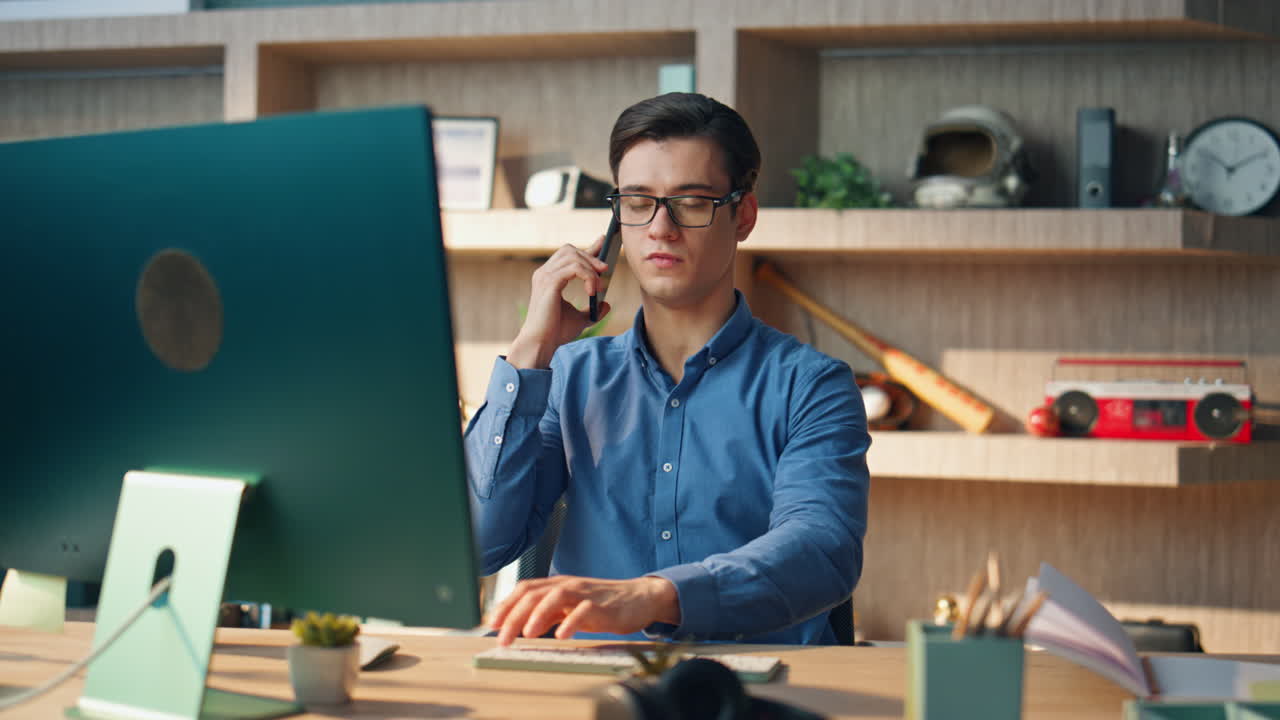 Primer plano de emprendedor serio llamando por teléfono en una oficina corporativa. Hombre escribiendo en el teclado.