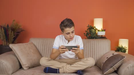 niño adicto al teléfono juega juegos en el teléfono en casa