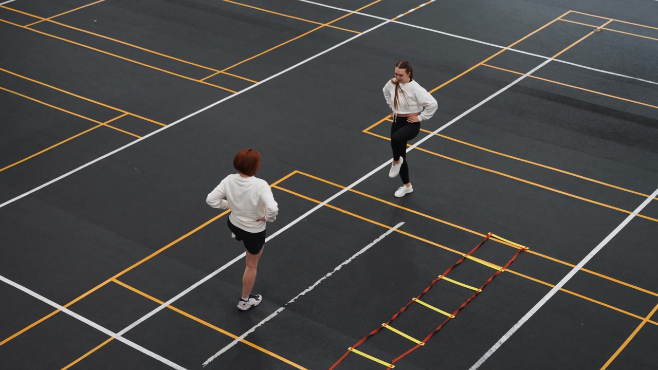 Two players doing badminton footwork drills outdoors, high intensity agility and speed session with lunges and sprints across grid markings, overhead angle captures motion, timing and endurance focus